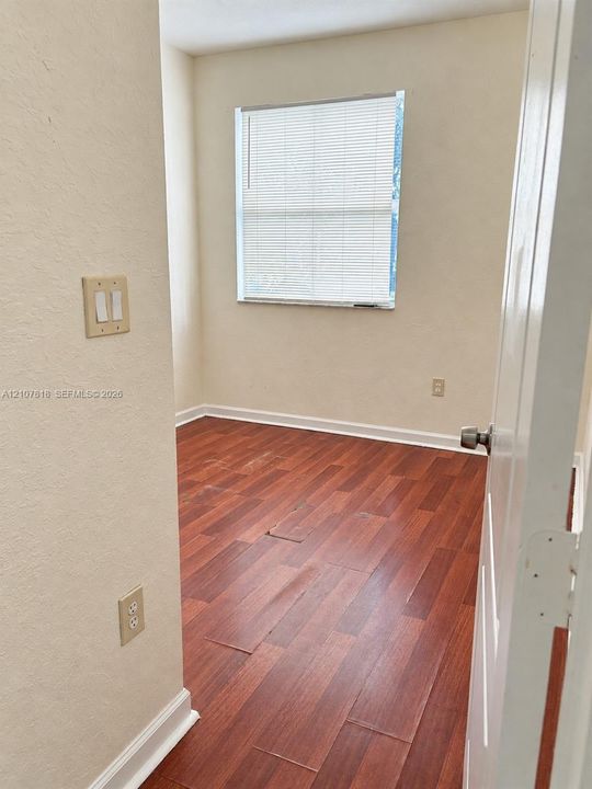 Room featuring wood-finish flooring, neutral-toned walls, and a single-pane window with installed blinds