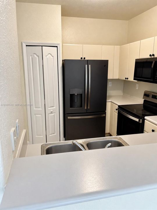 Kitchen featuring off-white cabinetry, black finish appliances, a dual-basin stainless steel sink, solid-surface countertops, and a full-height pantry with bi-fold doors