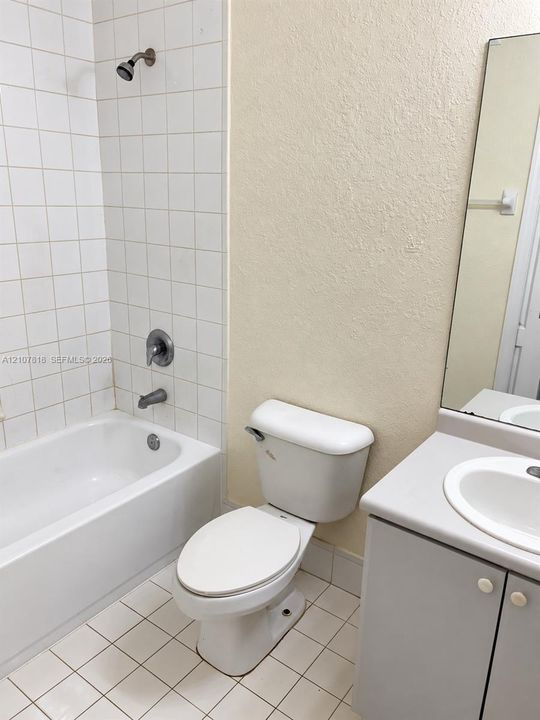 Bathroom featuring a tub-shower combination with white ceramic tile surround, integrated vanity cabinet with a solid surface countertop and undermount sink, and a wall-mounted mirror