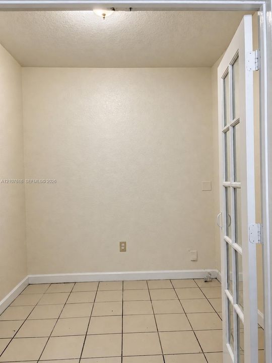 Neutral-toned interior space featuring square ceramic tile flooring, a white-framed French door with glass panels, and a ceiling-mounted light fixture