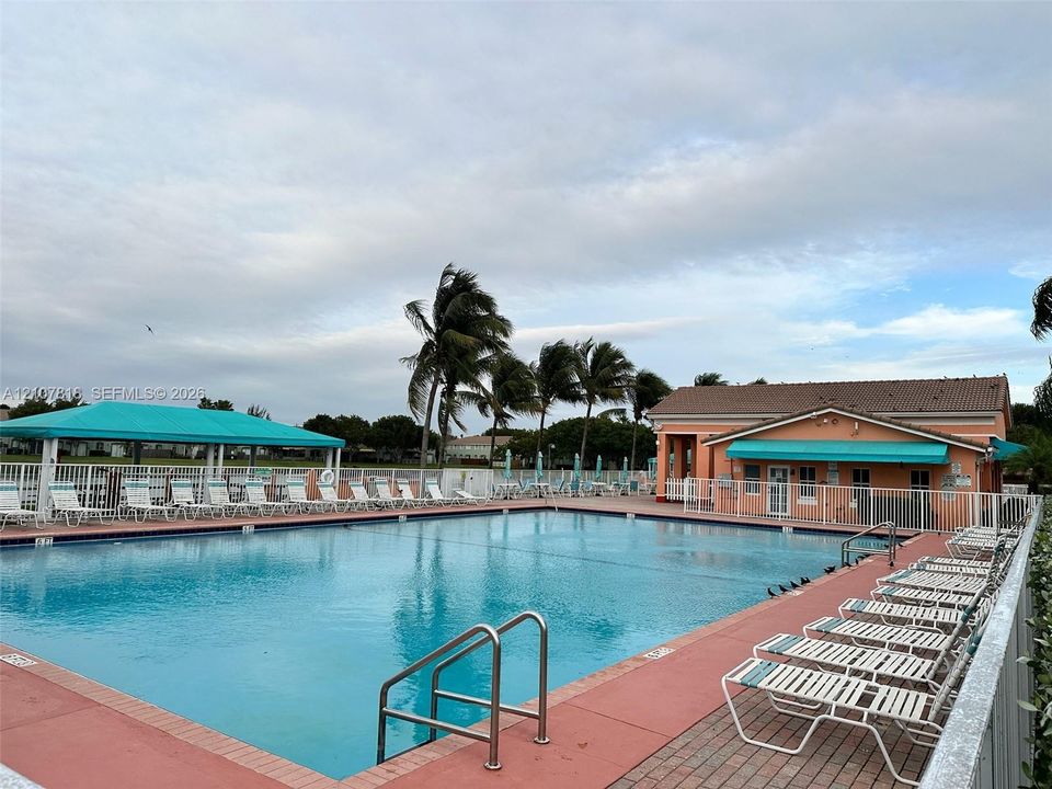 In-ground swimming pool featuring a brick-paver deck, shaded canopy area, and metal safety fencing
