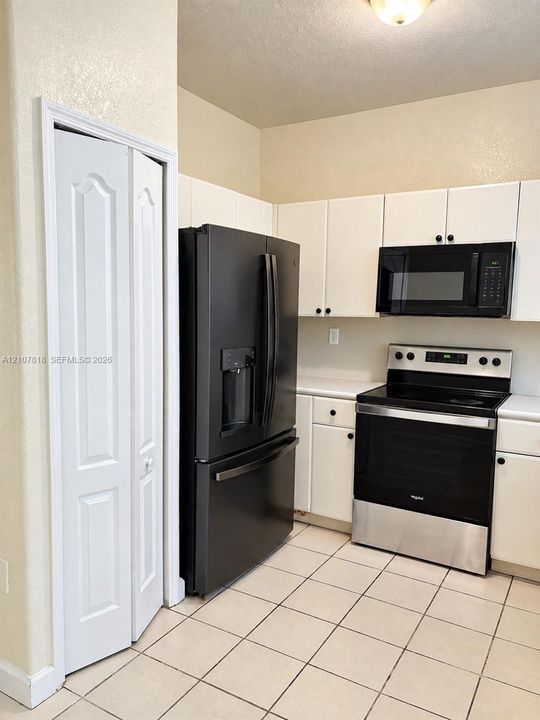 Kitchen featuring white cabinetry, ceramic tile flooring, a black French-door refrigerator, a black over-the-range microwave, and a stainless steel and black electric range