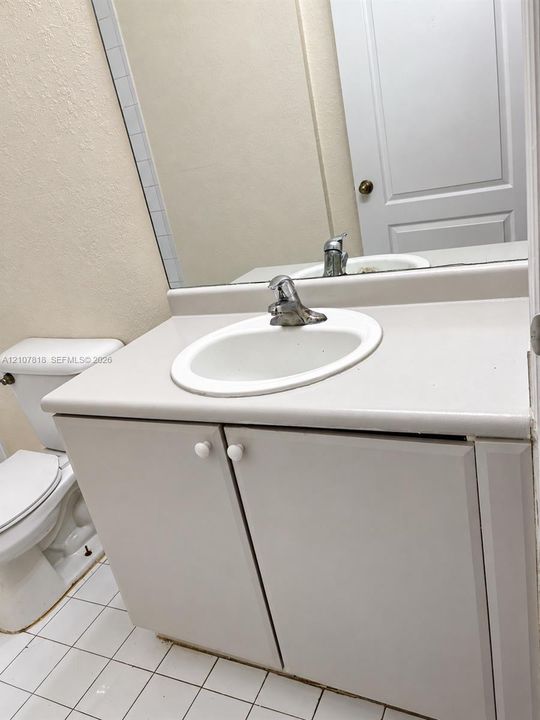 Bathroom vanity with a solid-surface integrated sink, chrome faucet, white cabinetry, and square ceramic tile flooring