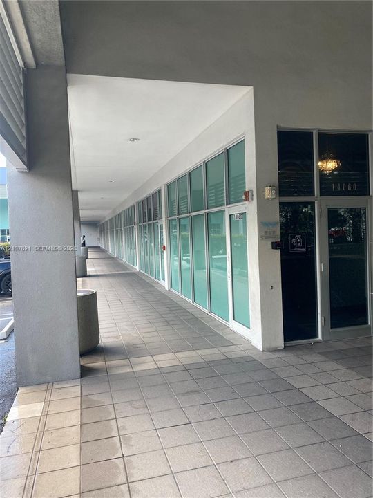 Covered exterior walkway featuring large glass storefront windows, tile flooring, and a recessed ceiling with integrated lighting