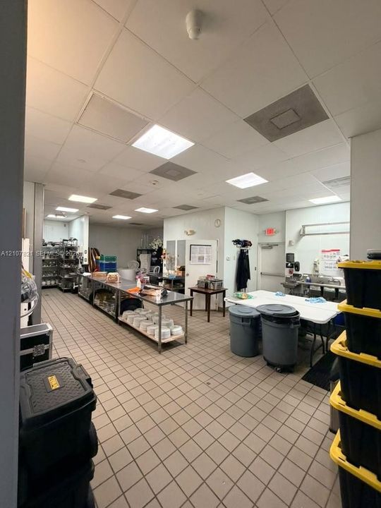 Commercial kitchen workspace featuring durable tile flooring, recessed drop-ceiling lighting, and stainless steel preparation surfaces