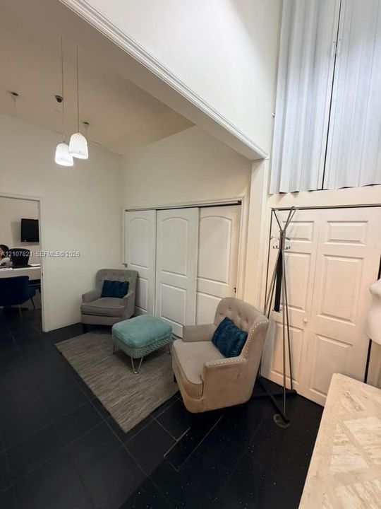 High-ceilinged room featuring dark tile flooring, multi-panel sliding closet doors with arched detailing, and dual pendant light fixtures