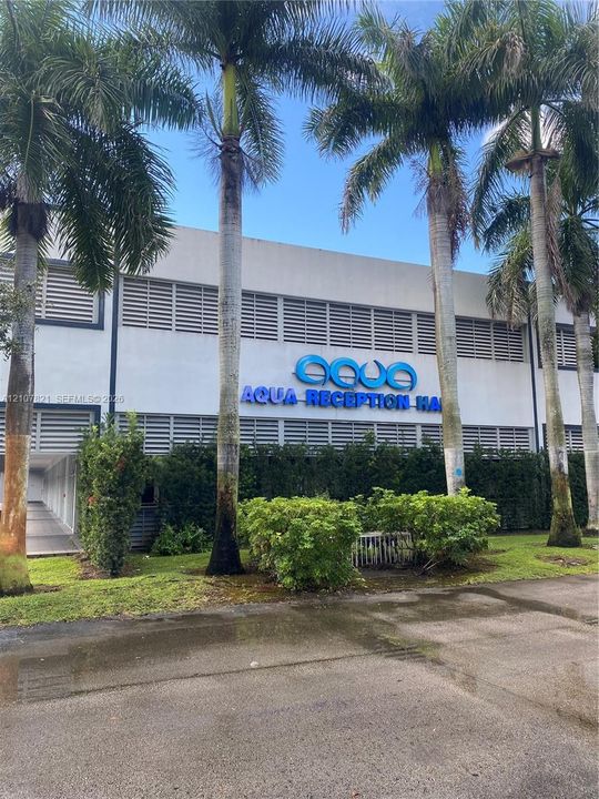 Commercial exterior featuring horizontal louvered window detailing, manicured shrubbery, and mature palm trees