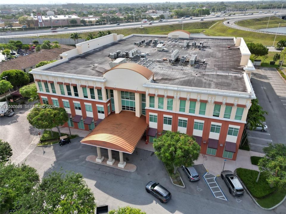 Three-story commercial building featuring a curved metal portico entrance, masonry facade with multi-pane windows, and paved surface parking