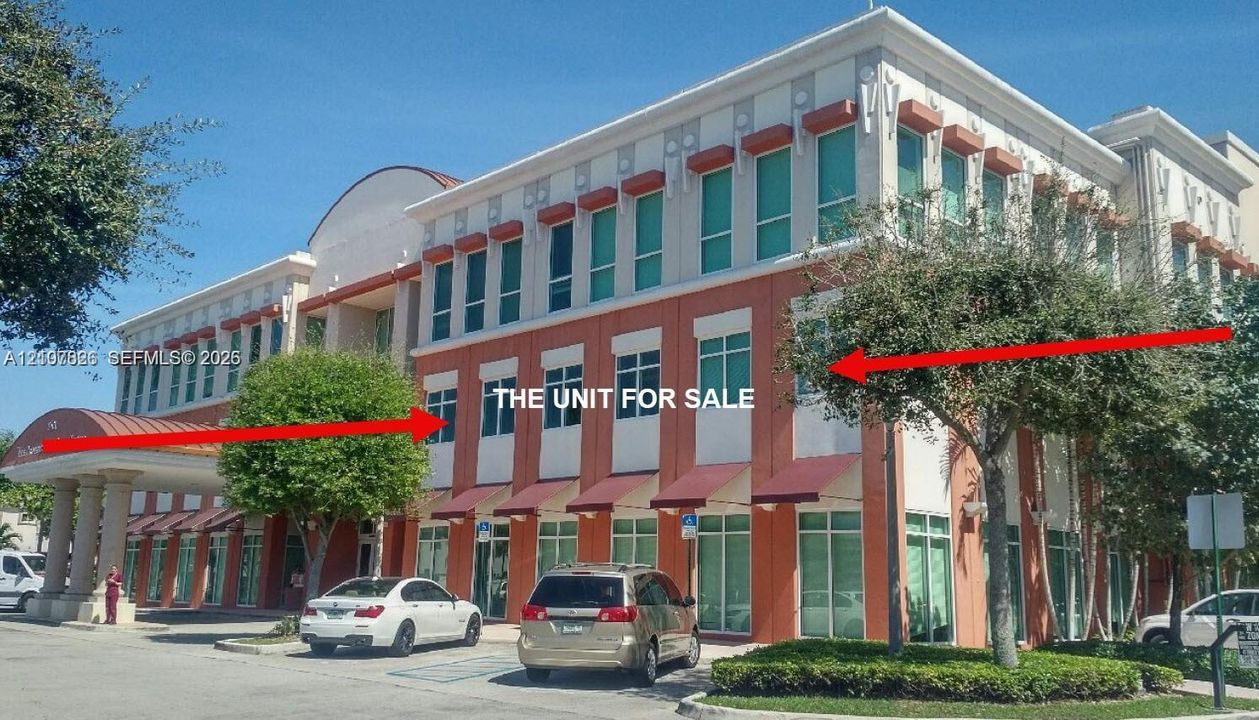 Commercial building exterior featuring a multi-story facade with expansive glass windows, structured red metal awnings, and a covered portico entrance supported by columns