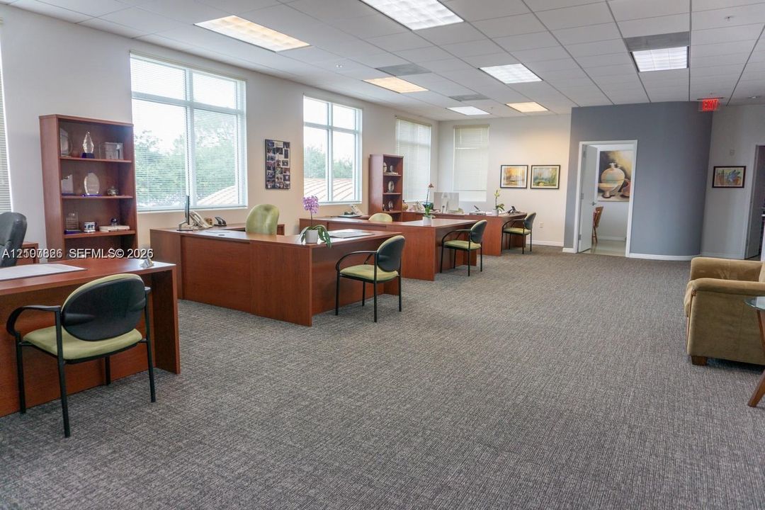 Open-plan interior featuring carpeted flooring, drop ceiling with recessed lighting, and large windows