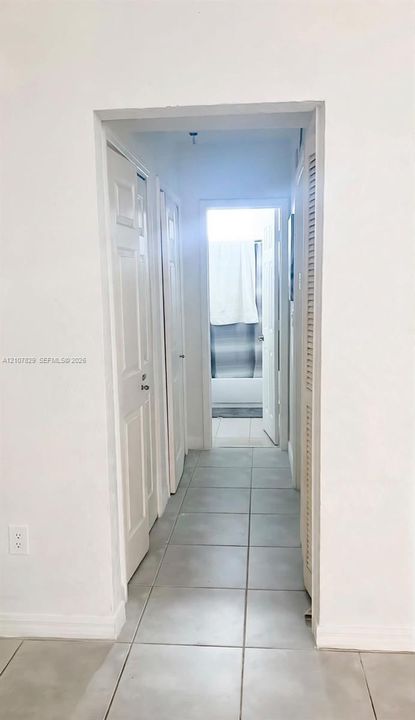 Hallway featuring large-format tile flooring, multiple six-panel interior doors, and built-in louvered closet cabinetry