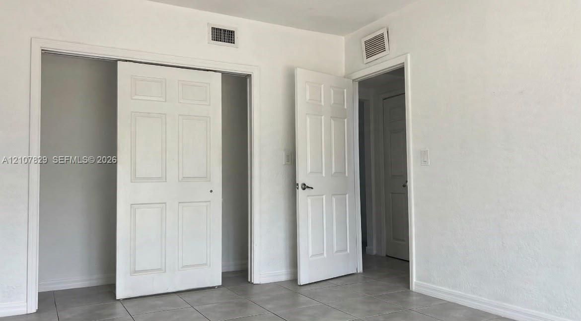 Neutral-toned interior space featuring light-colored tile flooring, smooth wall finishes, and multiple six-panel interior doors