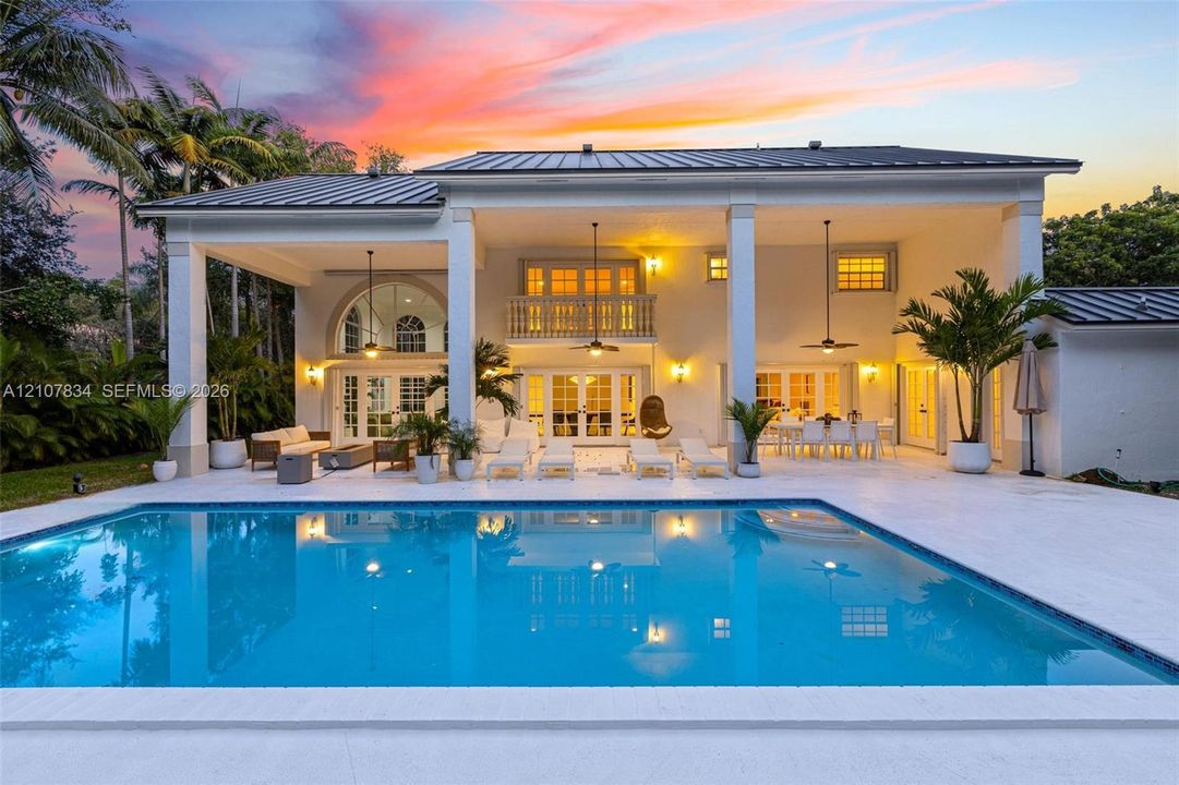 Custom rectangular swimming pool with stone decking, expansive covered patio, metal roofing, and second-story balcony