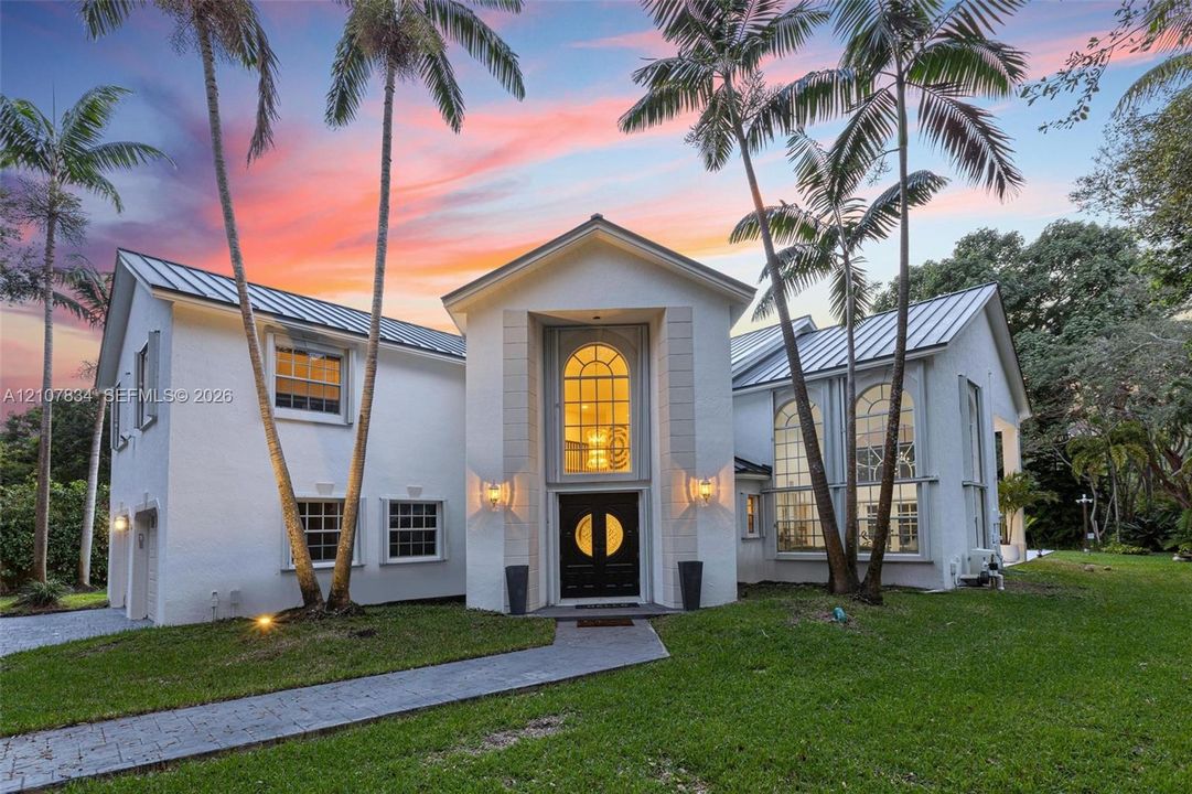 Stucco exterior featuring a metal roof, arched windows, grand double-door entrance, and a paved walkway