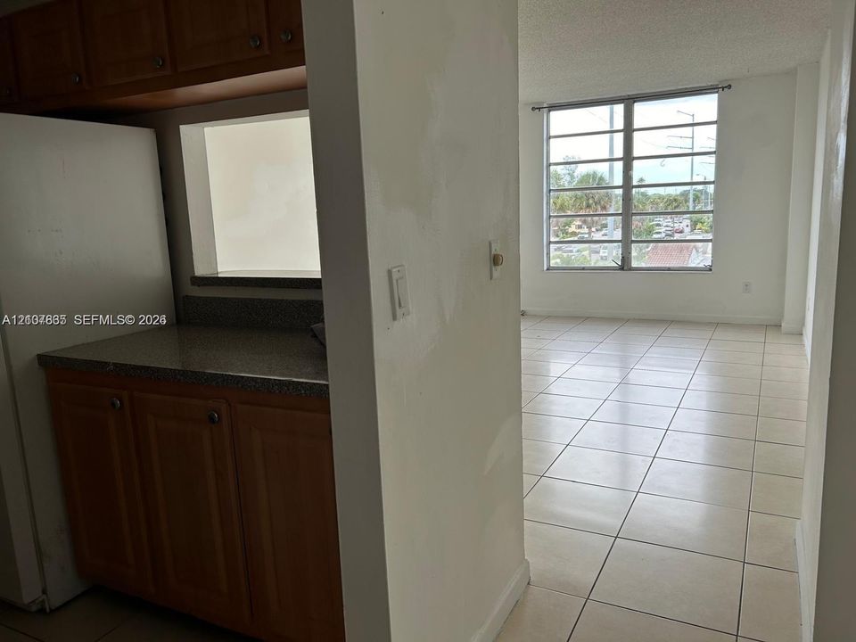 Kitchen featuring wood cabinetry, stone-finish countertops, and a pass-through window, paired with tile flooring throughout the area and large windows