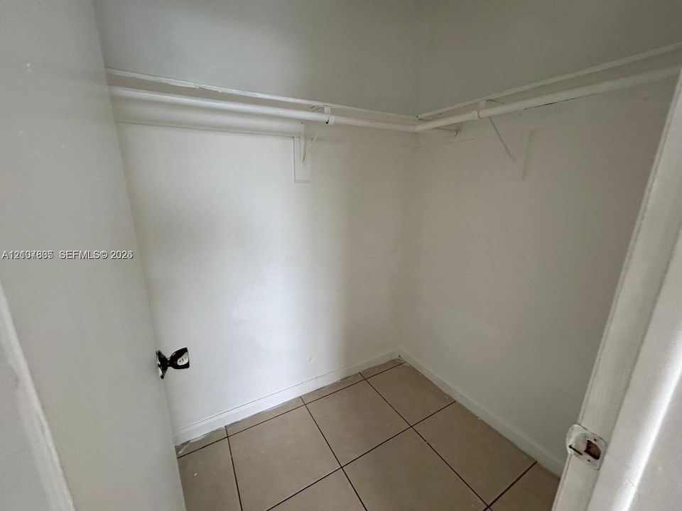 Storage space featuring large-format ceramic tile flooring, neutral wall finishes, and mounted white shelving rods