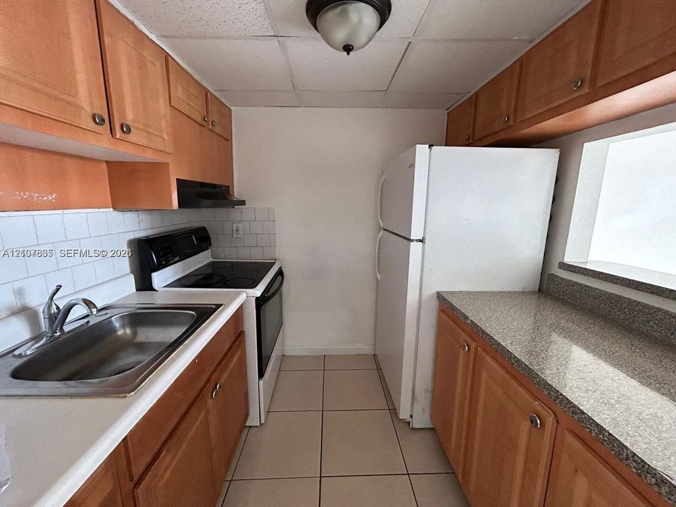 Kitchen featuring wood cabinetry, stone-finish countertops, tile backsplash, stainless steel sink, and ceramic tile flooring