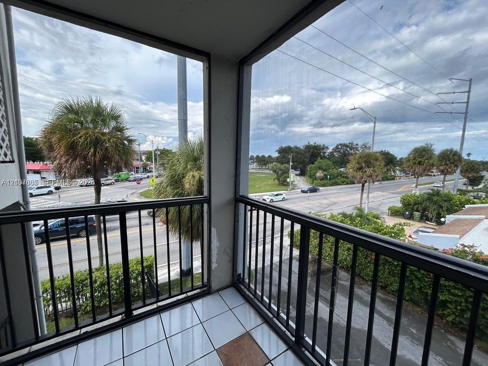 Covered balcony featuring screen enclosure, black metal railings, and tile flooring