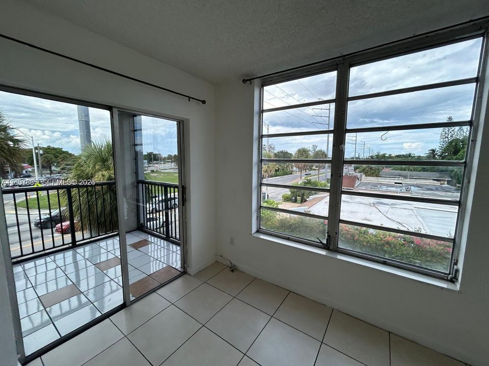 Interior space featuring ceramic tile flooring, floor-to-ceiling multi-pane metal windows, and a sliding glass door providing access to a private balcony with metal railing