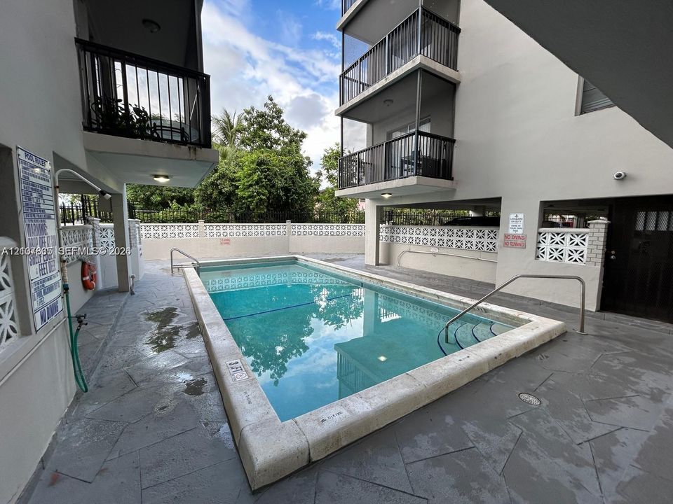 Swimming pool featuring stone-tile decking, a concrete perimeter coping, metal railings, and a decorative block masonry privacy wall