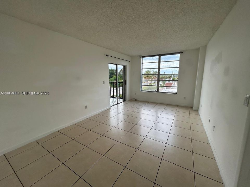Neutral-toned ceramic tile flooring, large multi-pane windows, and a sliding glass door providing external access to a railed balcony