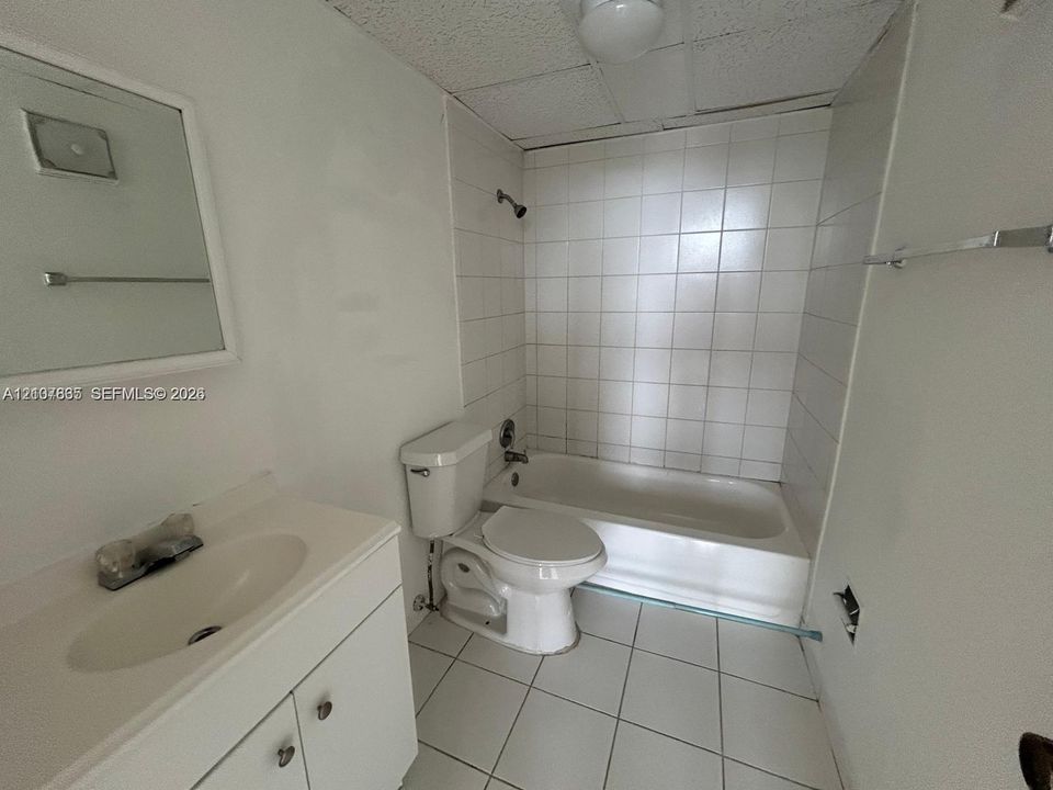 Bathroom featuring a white vanity with an integrated sink, white tile wall surround, standard bathtub, tiled flooring, and a wall-mounted mirror