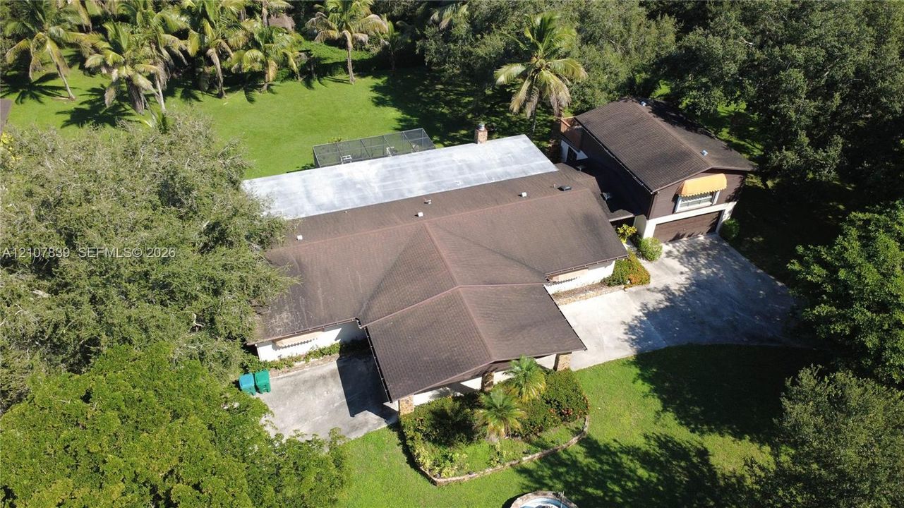 Aerial perspective of a multi-level residence featuring a multi-pitched roof, paved driveway, mature trees, and an expansive lawn