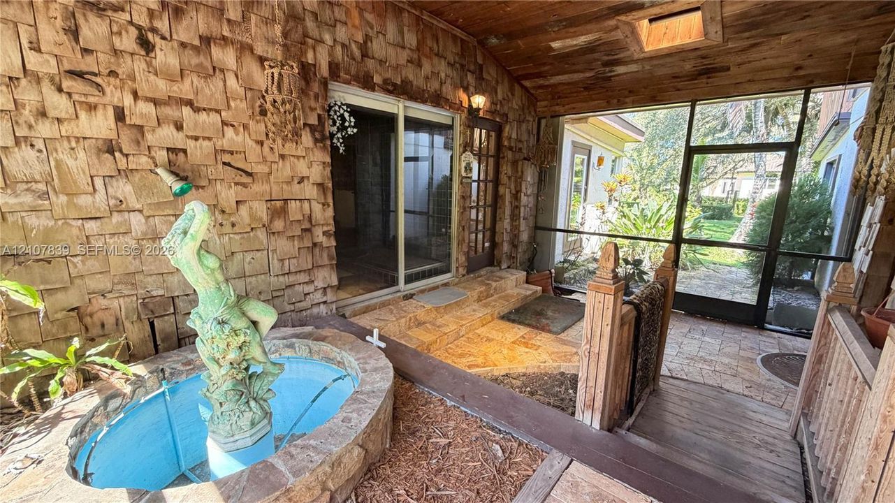 Screened-in porch featuring wood-shingle siding, a stone-accented fountain, wood-plank ceiling with skylight, and stone tile flooring