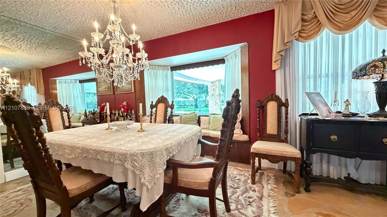 Formal dining area featuring a crystal chandelier, built-in window seating, wall-to-wall mirror paneling, and natural stone flooring