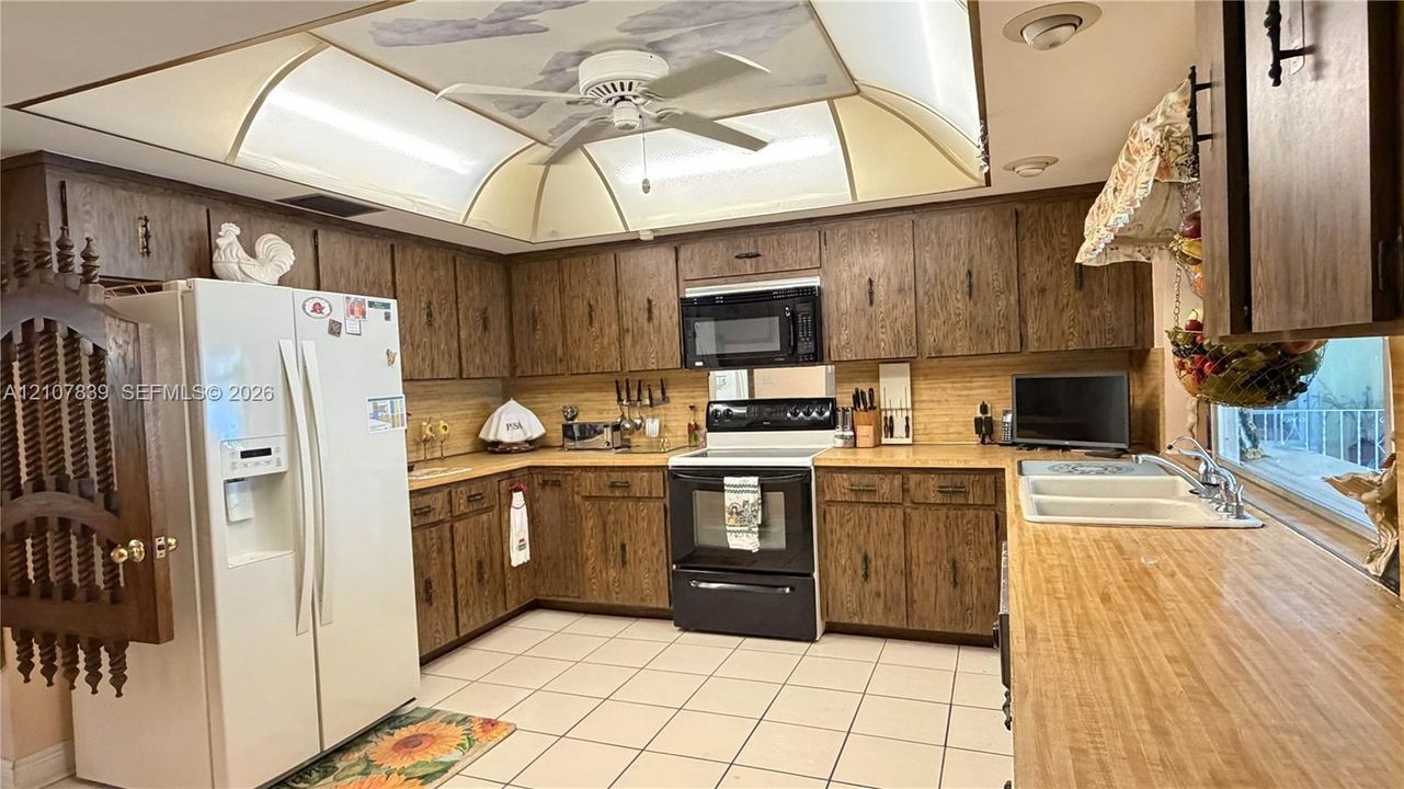 Kitchen featuring wood-finish cabinetry, built-in microwave, integrated range, dual-basin sink, and recessed tray ceiling with ceiling fan
