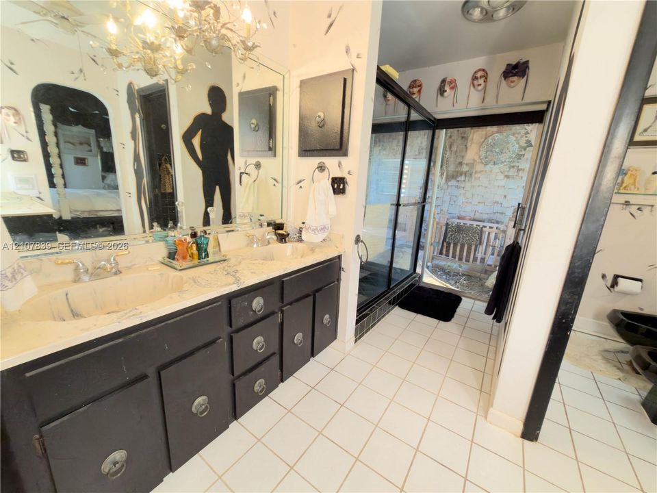 Double vanity with stone countertop, dual undermount sinks, black cabinetry with ring-pull hardware, and glass-enclosed shower with black trim