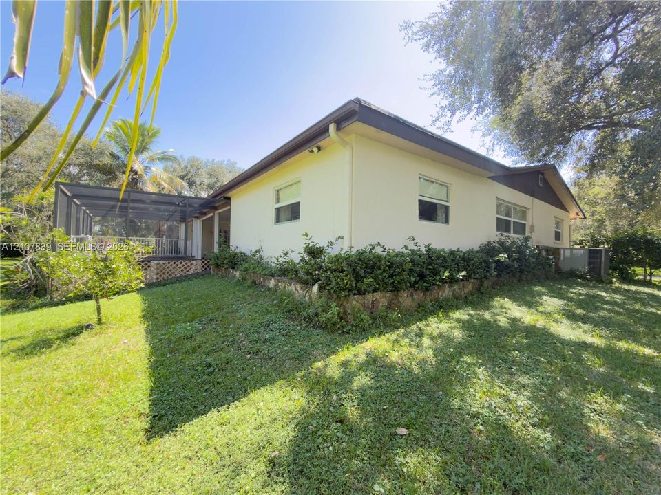 Stucco exterior featuring a screened-in lanai, stone-accented landscaping, and mature trees on a lot with expansive lawn space