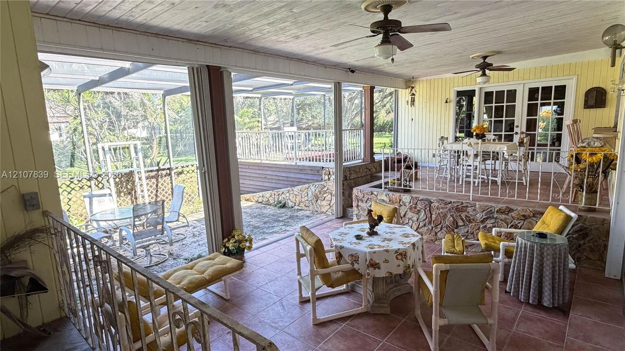 Covered patio featuring ceramic tile flooring, stone-veneer retaining wall, white metal railing, and dual ceiling fans