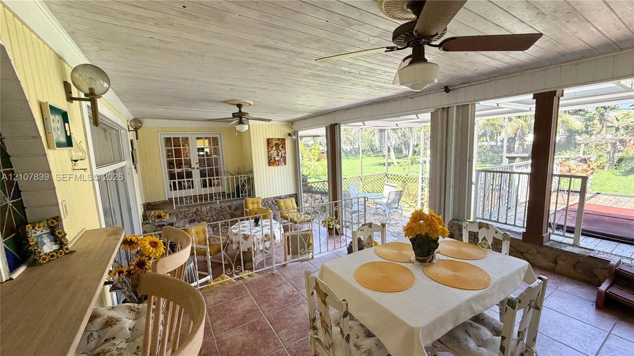 Enclosed sunroom featuring tile flooring, beadboard wood-paneled ceiling, ceiling-mounted fans, wall-mounted light fixtures, and a metal railing partition