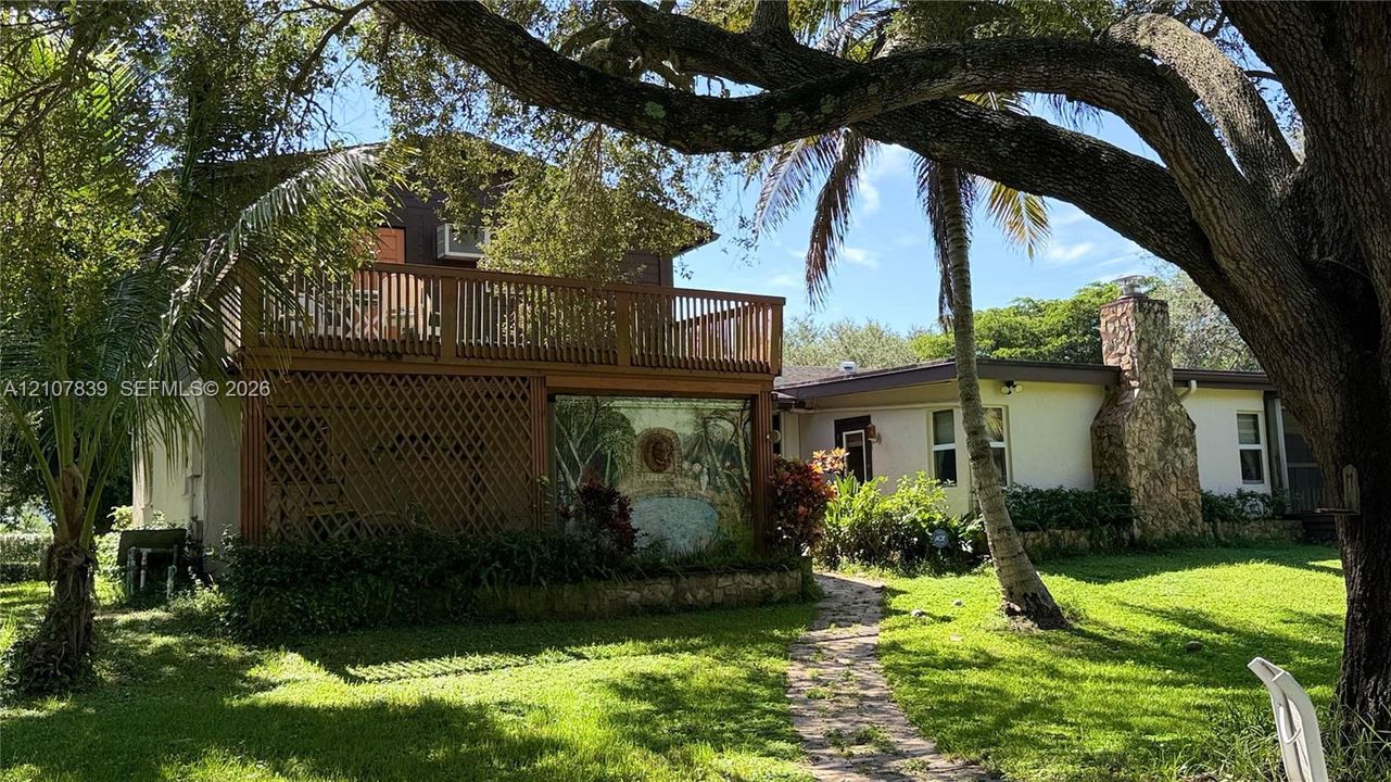 Exterior featuring a two-story wood balcony with railings, a stone masonry chimney, and a stone-paved path set within a landscaped lawn