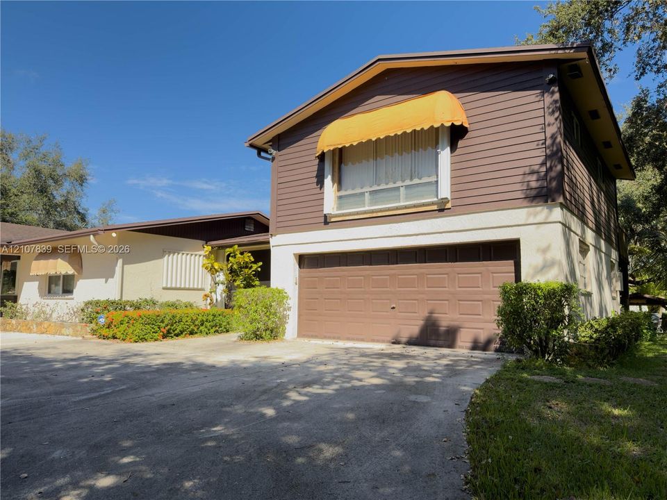 Two-story residence featuring lap siding, an attached two-car garage, fixed exterior window awnings, and a paved driveway