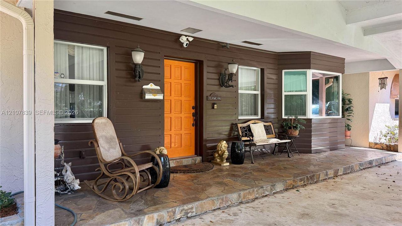 Covered entryway featuring horizontal siding, natural stone flooring, a multi-panel door, and wall-mounted exterior lighting