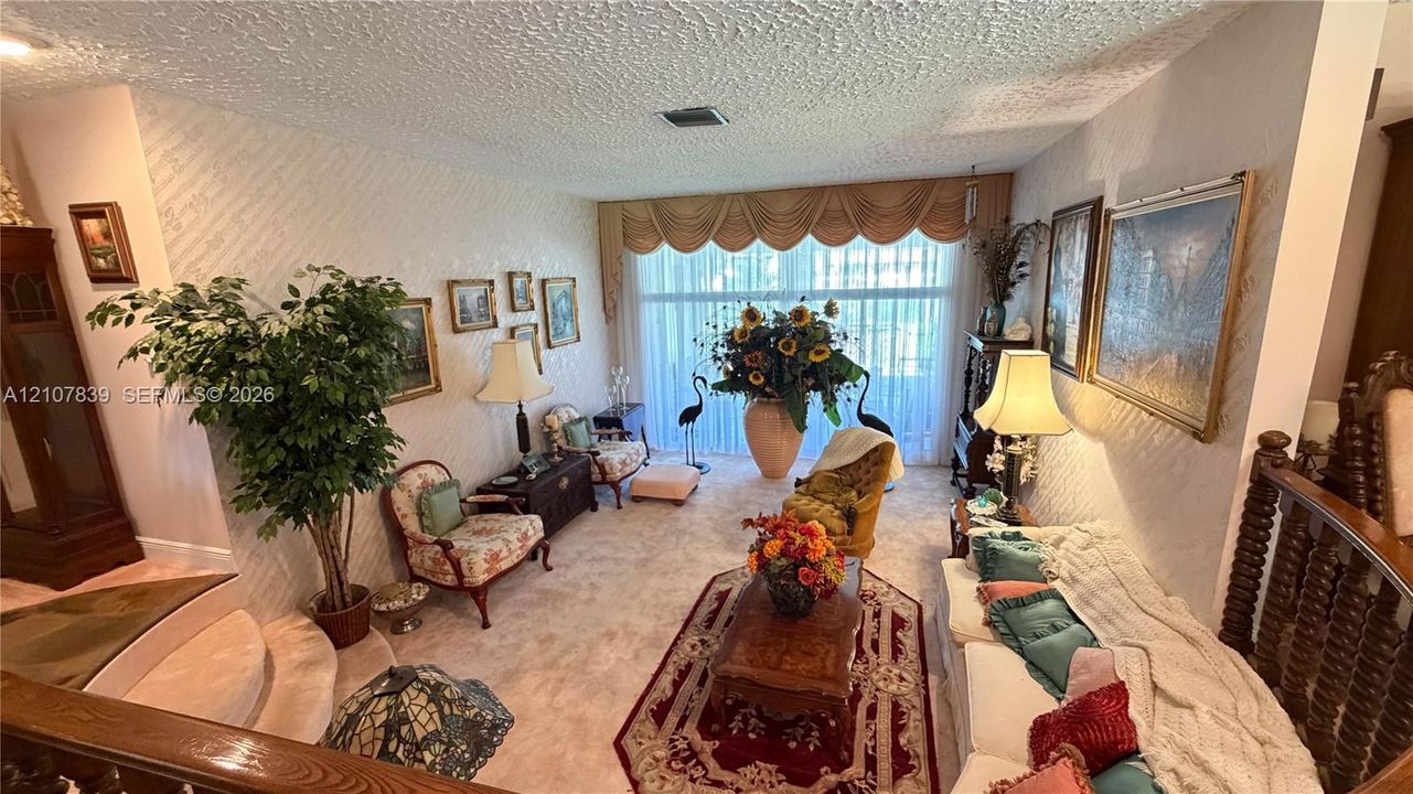 Living area featuring wall-to-wall carpeting, textured wall finishes, and floor-to-ceiling windows with integrated valance