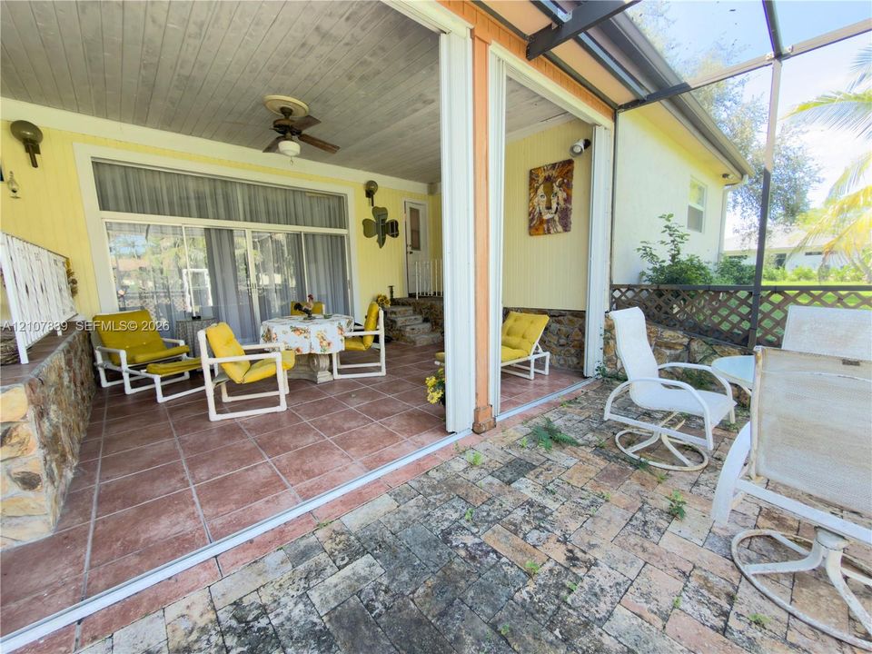 Covered patio featuring ceramic tile flooring, ceiling fan, and stone-accented masonry, leading to an exterior paved brick terrace enclosed by screen paneling