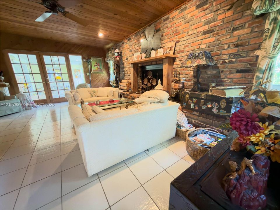 Exposed brick fireplace with a wood mantel, wood-plank ceiling, ceramic tile flooring, and multi-pane glass doors