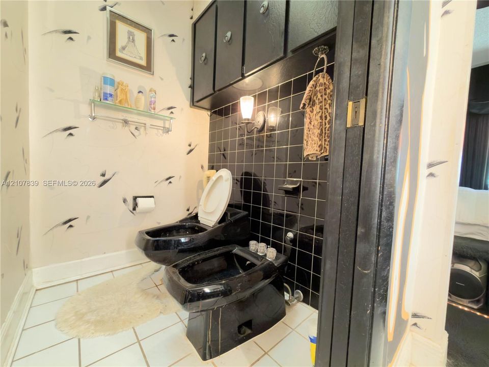 Black toilet and bidet fixture set, wall-mounted black cabinetry, black grid-pattern tile backsplash, and wall-mounted light fixture