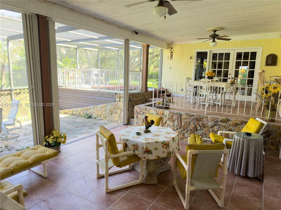 Covered porch featuring tile flooring, multi-panel sliding glass doors, stone-veneer retaining walls, and dual ceiling fans
