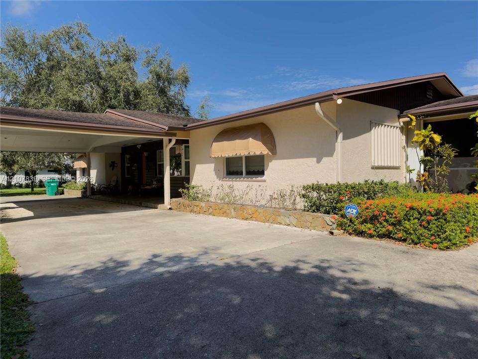 Single-story residence featuring a paved carport, stone-accented planter box, window awnings, and low-maintenance exterior siding