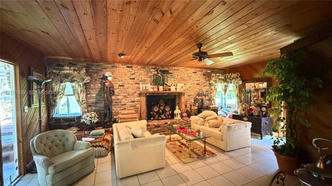 Wood-plank ceiling, exposed brick fireplace, diagonal wood-paneled walls, and tile flooring