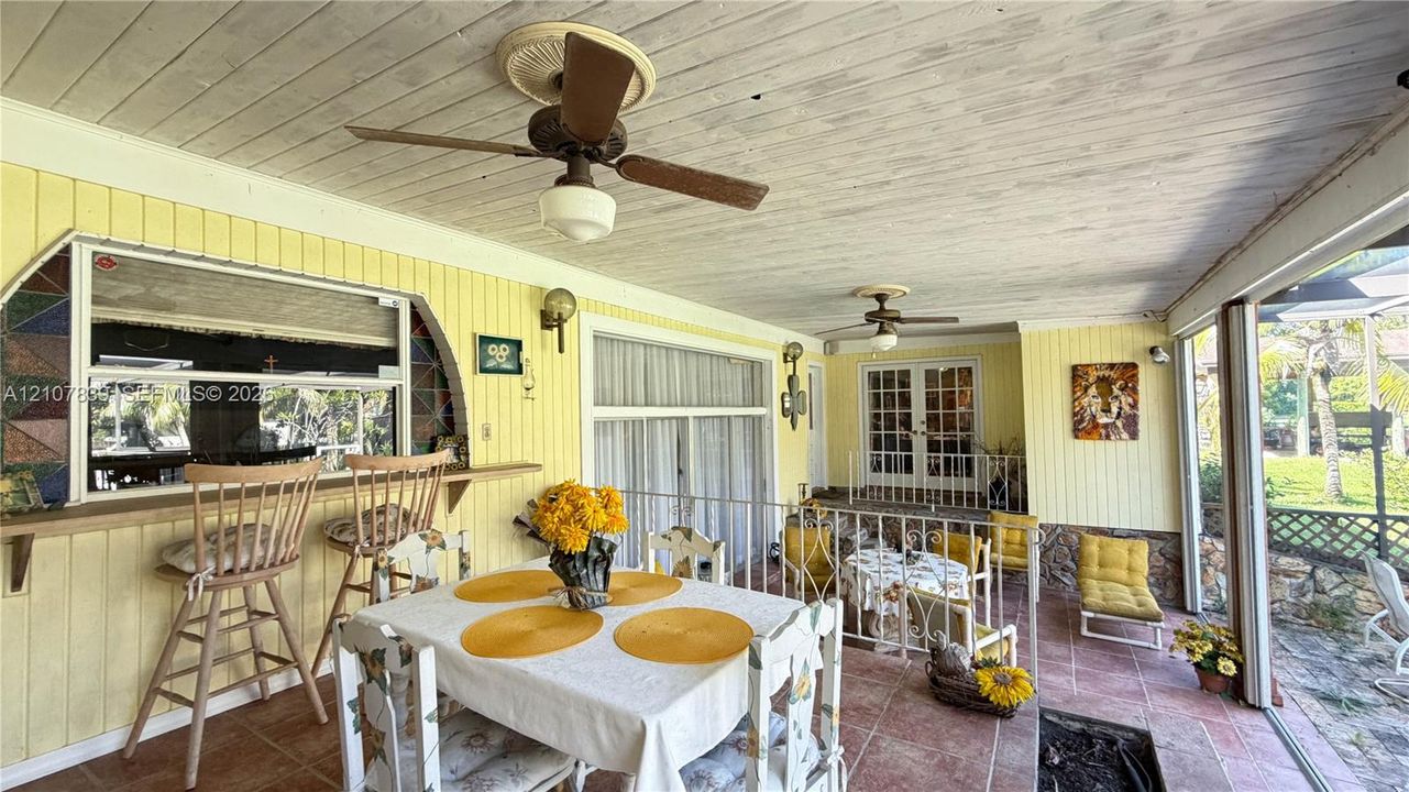 Covered patio featuring ceramic tile flooring, beadboard ceiling, built-in exterior bar counter, dual ceiling fans, and wrought iron railings