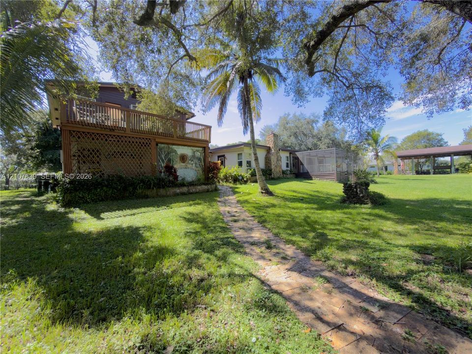 Expansive grounds featuring a natural stone pathway, mature trees, multi-level wood deck, stone-accented exterior, and detached covered parking structure