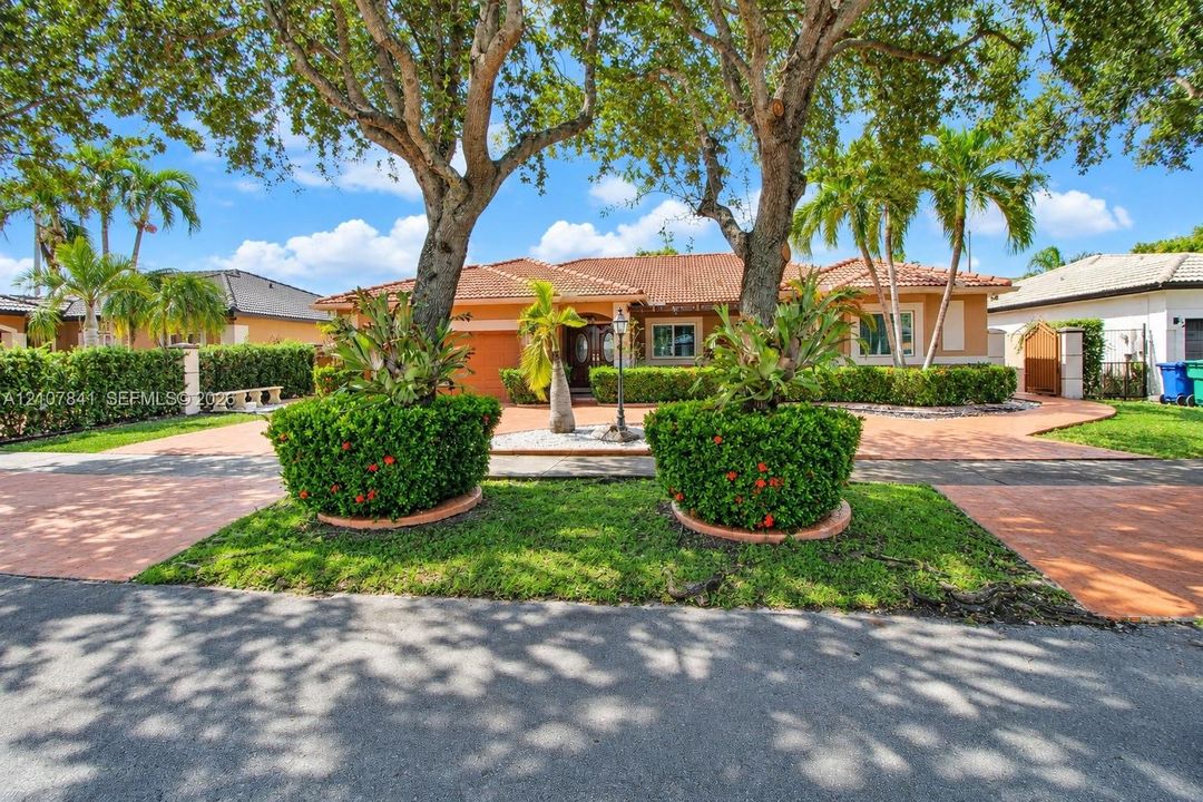 Single-story residence featuring a tile roof, paver driveway, mature landscaping, and palm trees