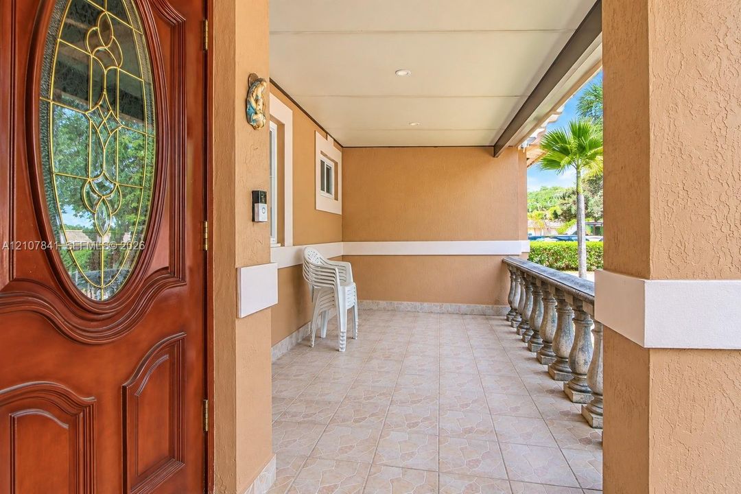 Covered front porch featuring tile flooring, stone-style balustrade railing, recessed ceiling lighting, and a solid wood entry door with an oval decorative glass insert