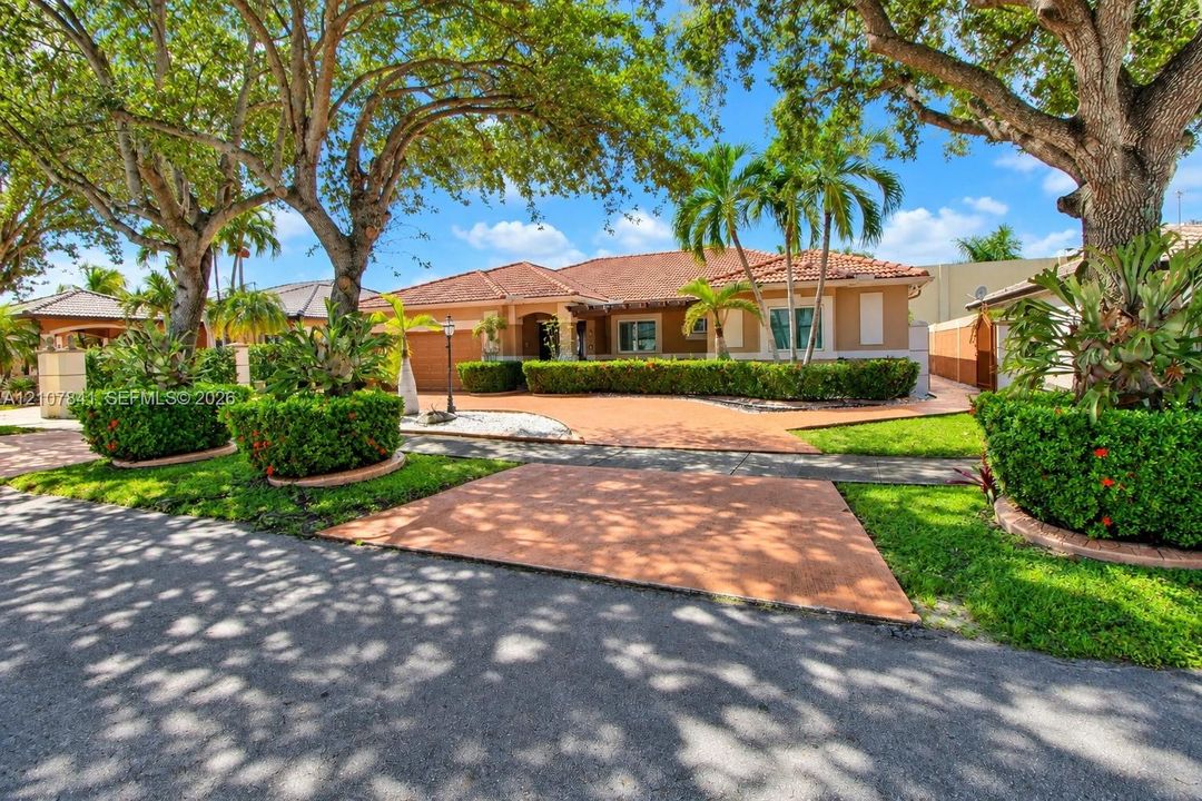 Single-story exterior featuring a clay tile roof, stucco facade, decorative hardscaping, and mature landscaping