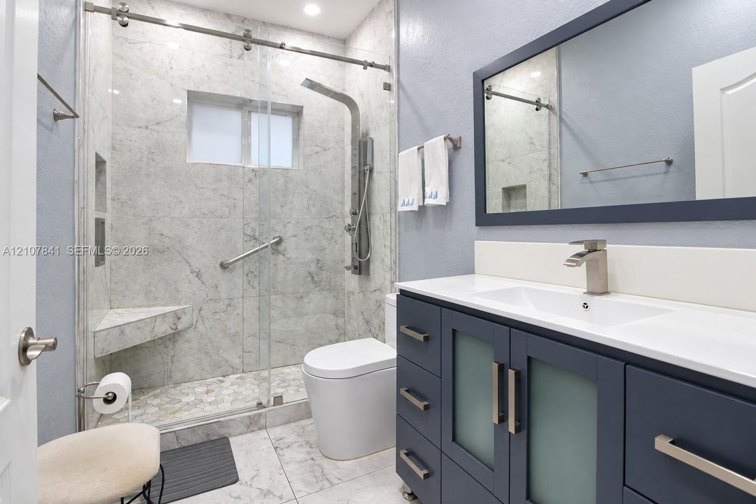 Bathroom featuring a vanity with blue cabinetry, a rectangular sink, stone-surround shower with a glass sliding door, and a built-in shower seat